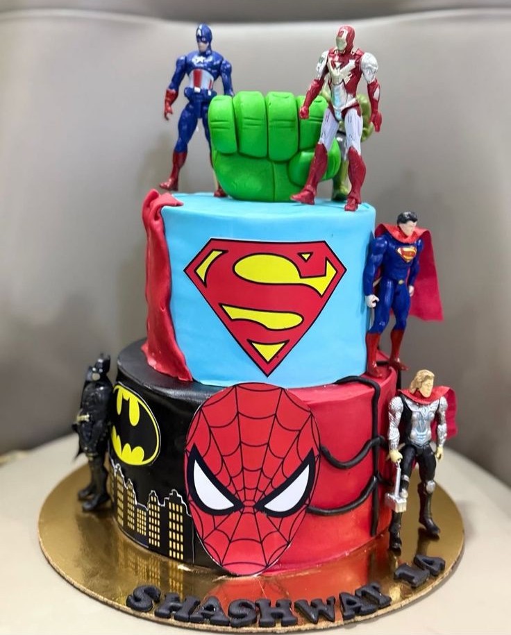 Superhero themed two-tier cake with comic logos and character toppers